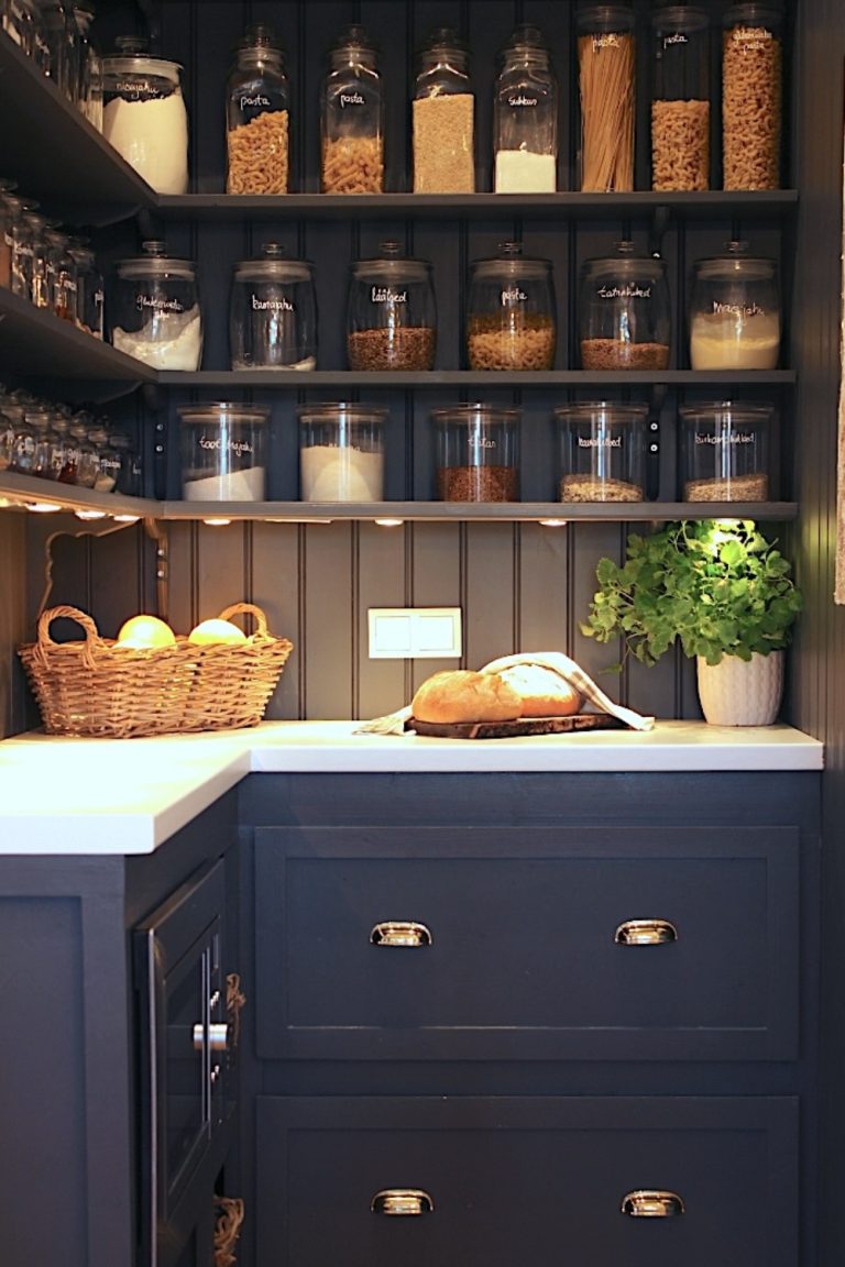 Organized pantry with labeled glass jars, wicker baskets, and wooden shelves in a moody, traditional style.